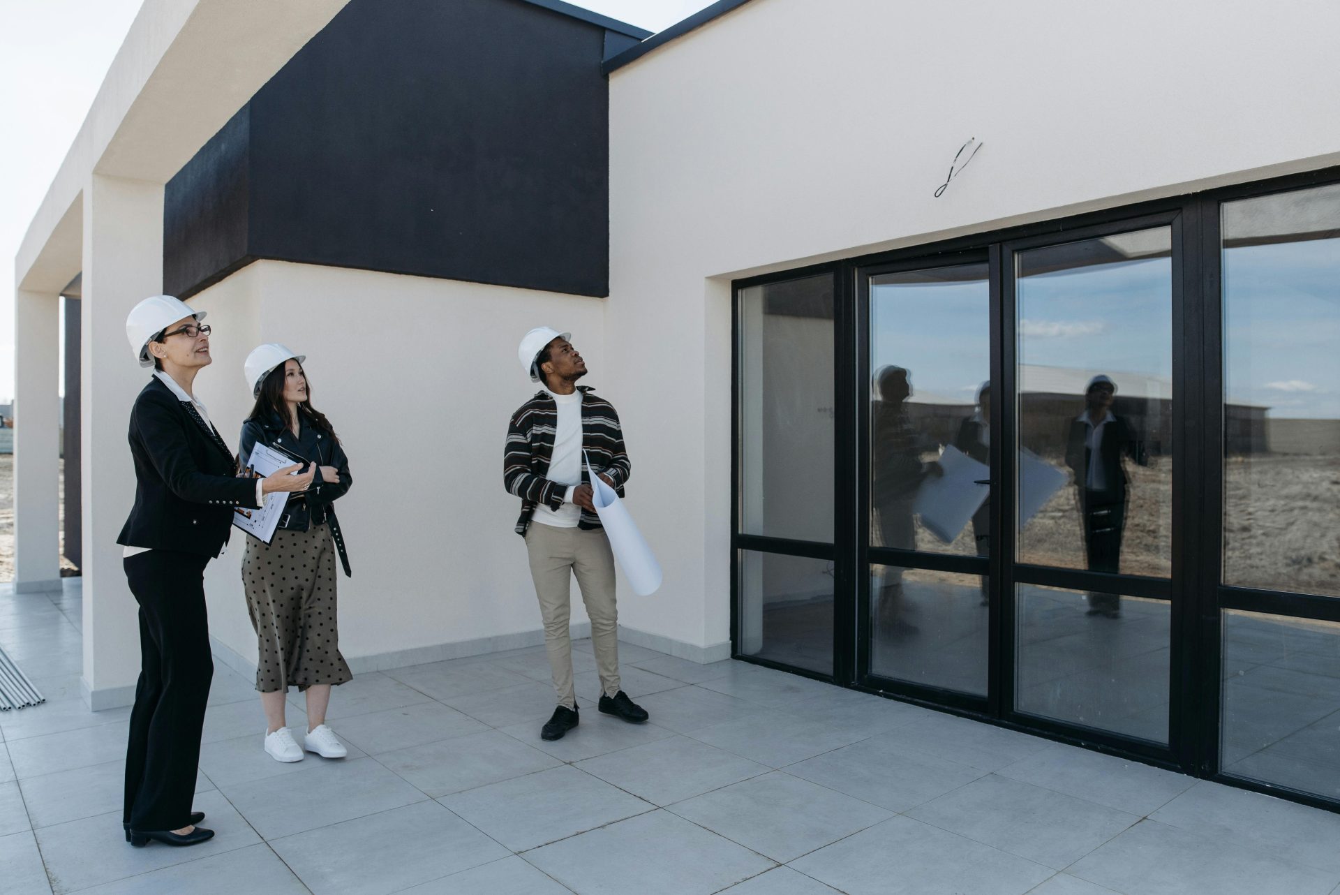 Des architectes casqués discutent de la structure d'un nouveau bâtiment doté de grandes portes vitrées, suggérant un design architectural moderne.