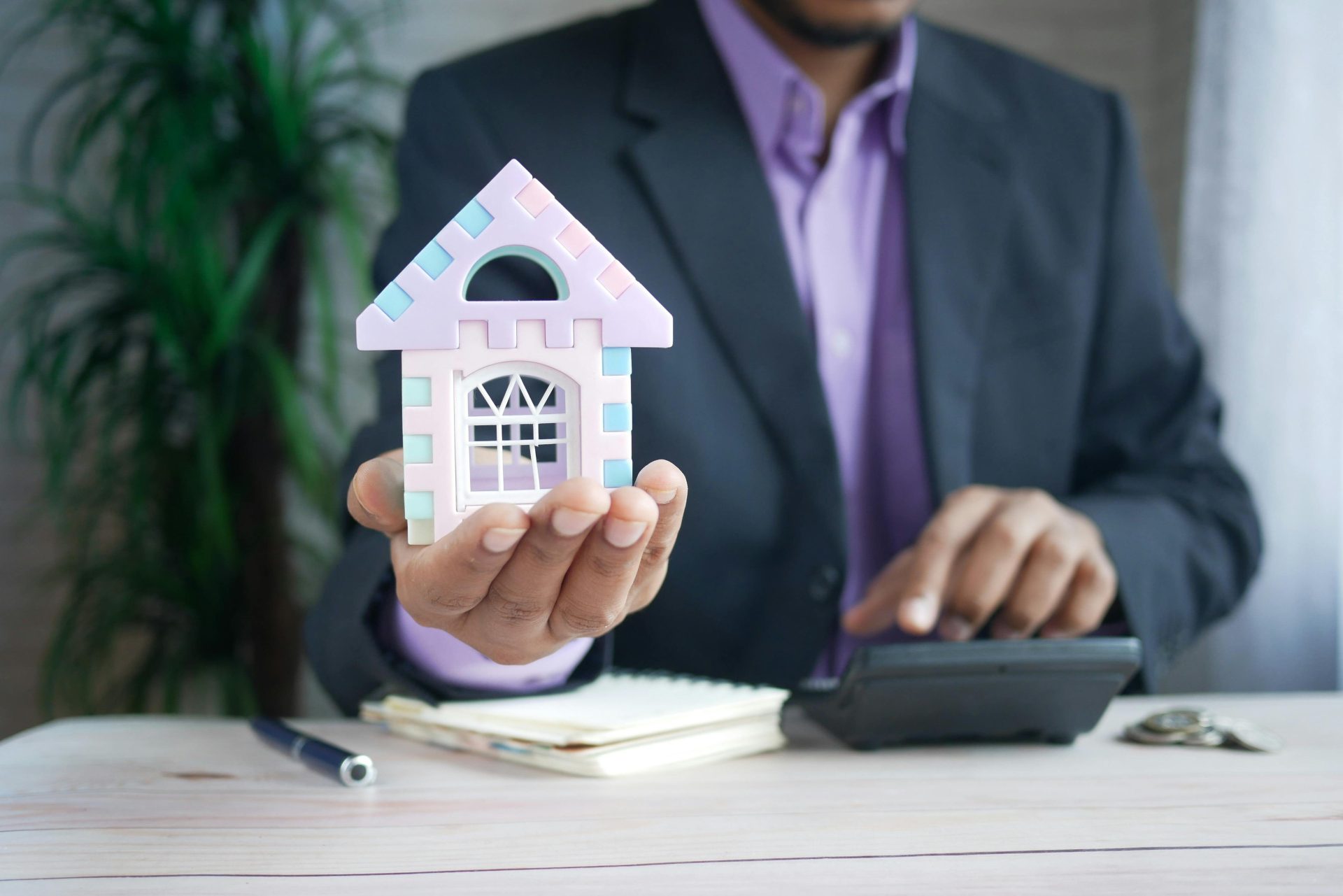 Geschäftsmann im Anzug hält ein Musterhaus in der Hand und berechnet Immobilieninvestitionen.